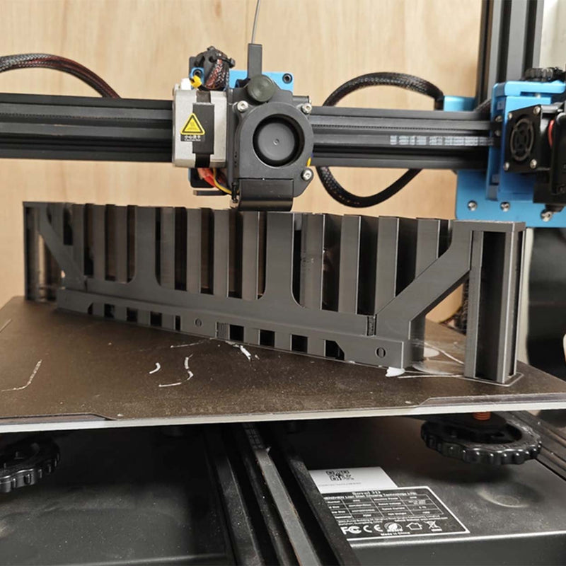 Zwarte geprinte kabelgoot op het bed van een Ender-printer met de printkop erboven